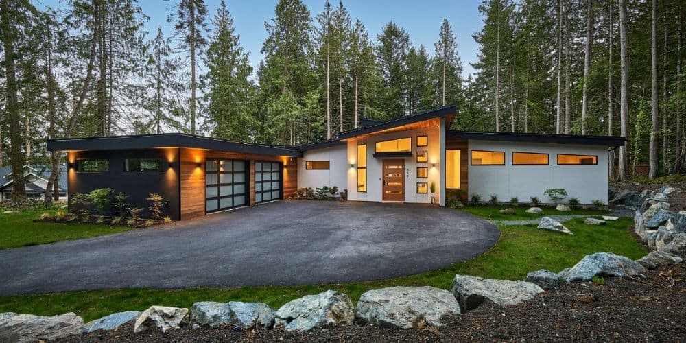 Modern custom home exterior in forest setting with stone landscaping and warm lighting.