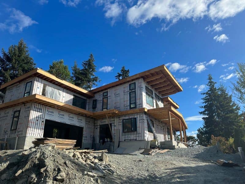 Under-construction home by White Wolf Homes in Victoria BC with lumber and framing on a sunny day.