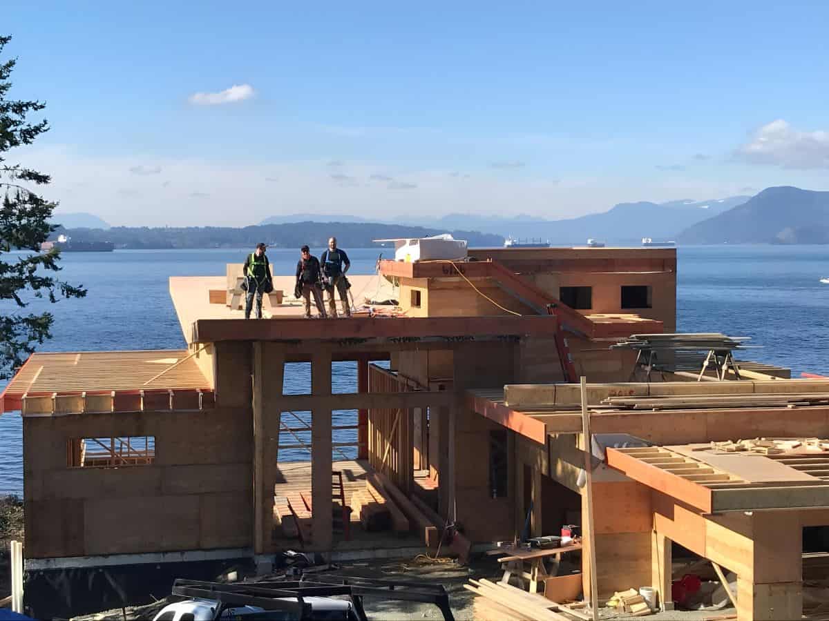 Construction workers on a wooden-frame home by the water with mountains in the distance, Victoria BC.