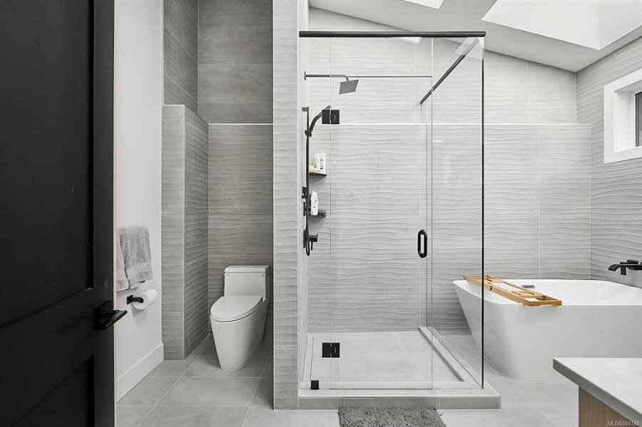 Modern glass shower enclosure in a grey tile bathroom with tub and toilet.