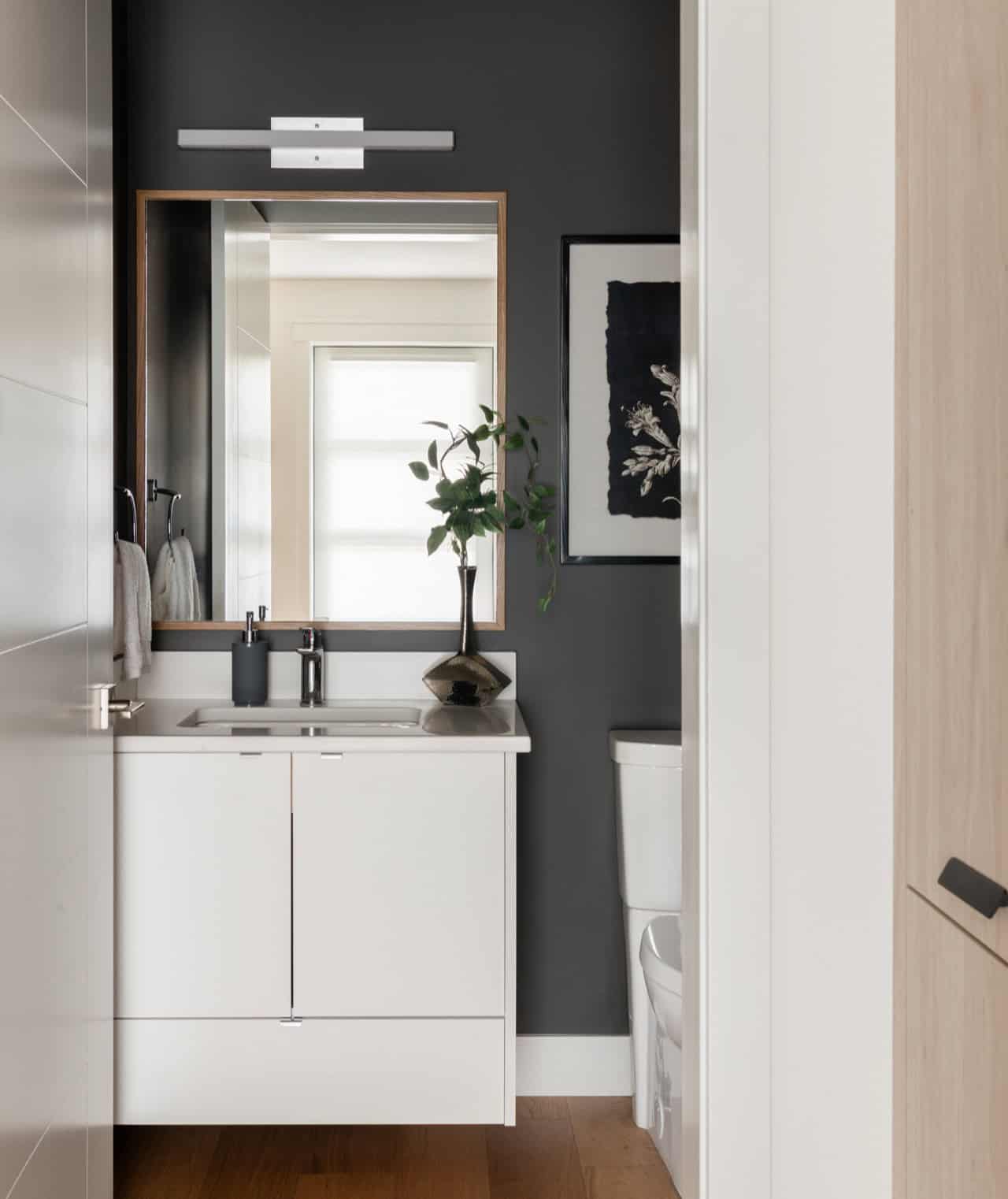 Modern bathroom vanity with white cabinetry, dark wall, and plants in Victoria BC home.