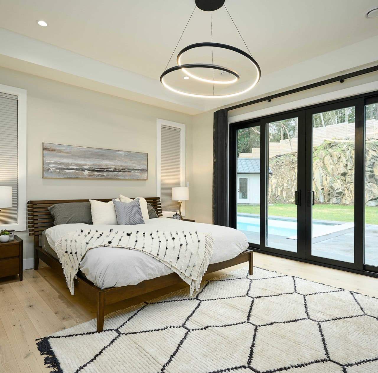 Modern bedroom with large glass doors and circular ceiling light in a bright airy room.