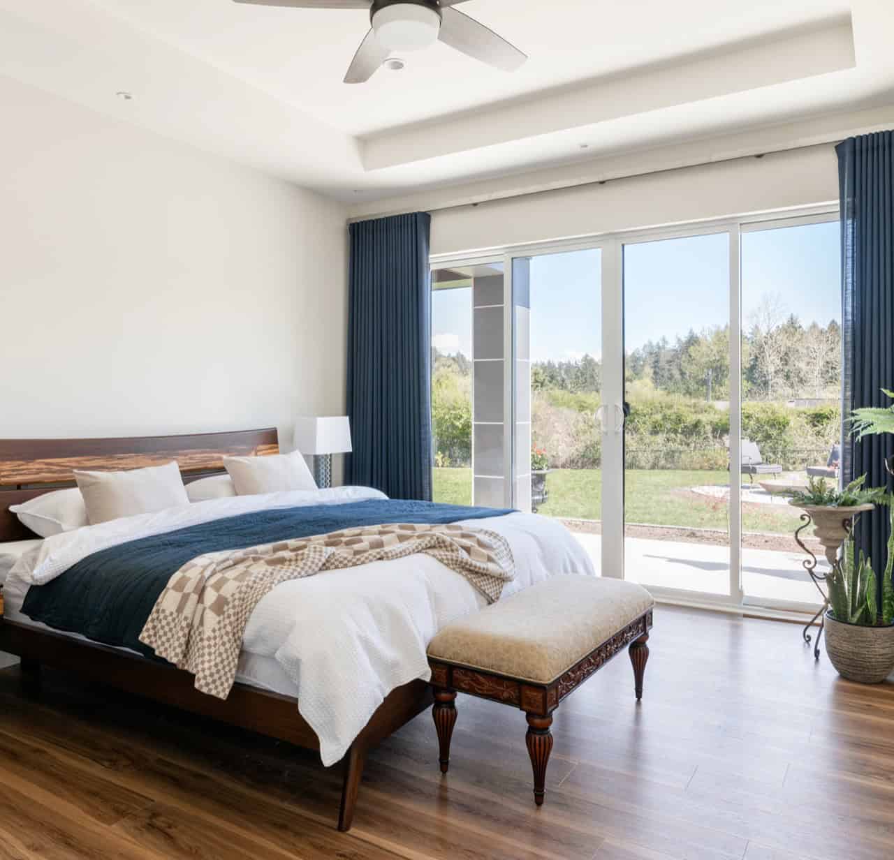 Spacious master bedroom with large glass doors to a patio and landscaped yard, and a contemporary queen bed.