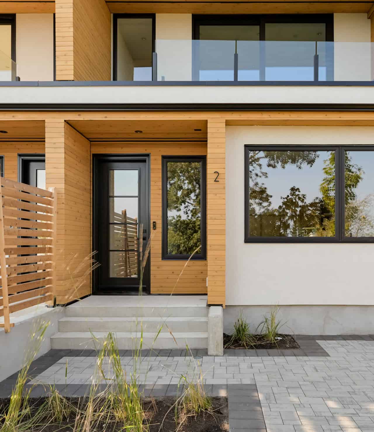 Modern two-story home entrance with wooden siding, black door, and large windows in Victoria BC.