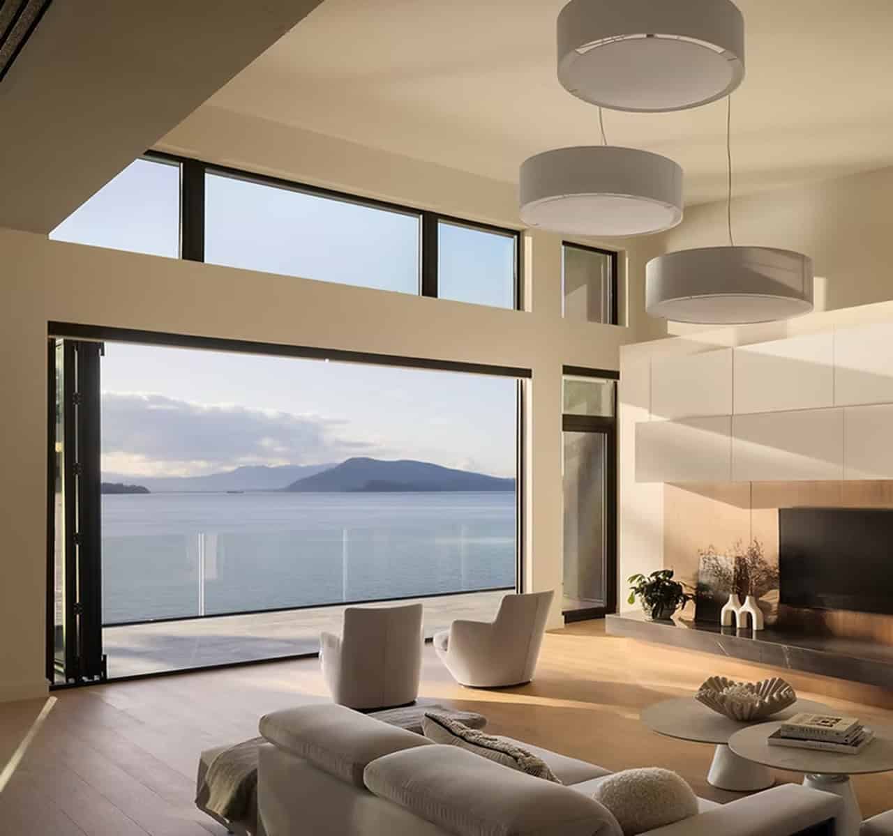 Bright living room with large glass doors overlooking water and distant islands, modern white decor.