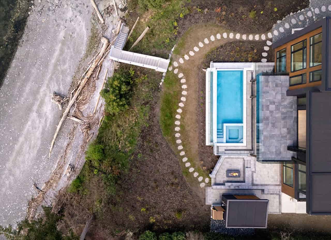 Aerial view of a modern villa by White Wolf Homes with a blue pool and stepping-stone path in a lush garden.