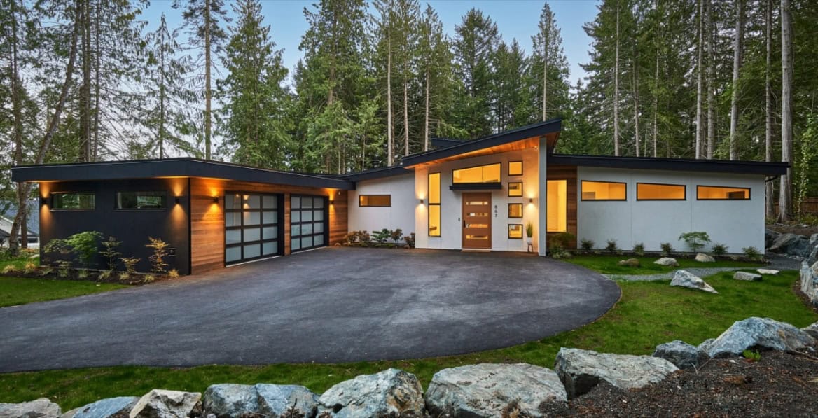 Modern custom home in Victoria BC by White Wolf Homes with expansive driveway and woodland backdrop.