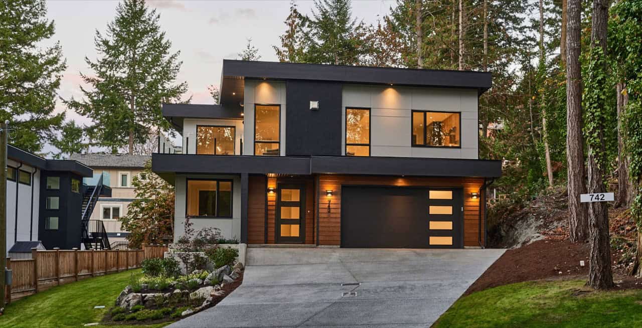 Modern two-story home with dark exterior, large windows and a double garage in a wooded setting.