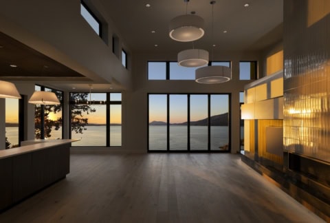 Modern interior with large windows overlooking water and sunset, open-plan living space by White Wolf Homes.