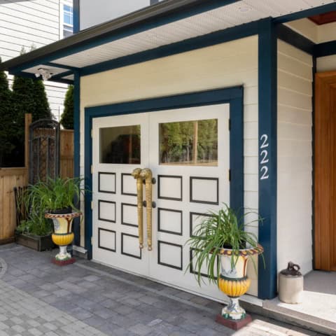 Modern white garage door with decorative panels and brass handles at a blue-trimmed home.