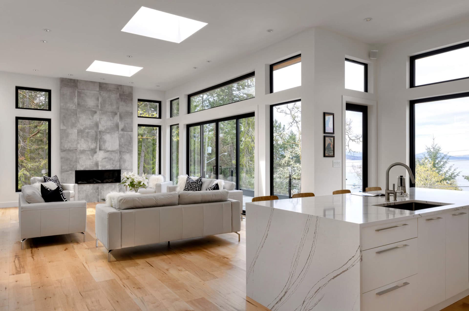 Bright open-concept living area with large windows and marble island, modern white furnishings.