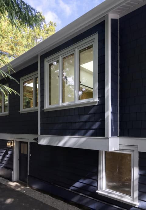 Blue modern home exterior with white-framed windows and shadowed landscaping.