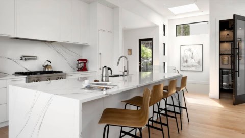 Modern white kitchen with marble countertops and wooden bar stools in a White Wolf Homes custom home.