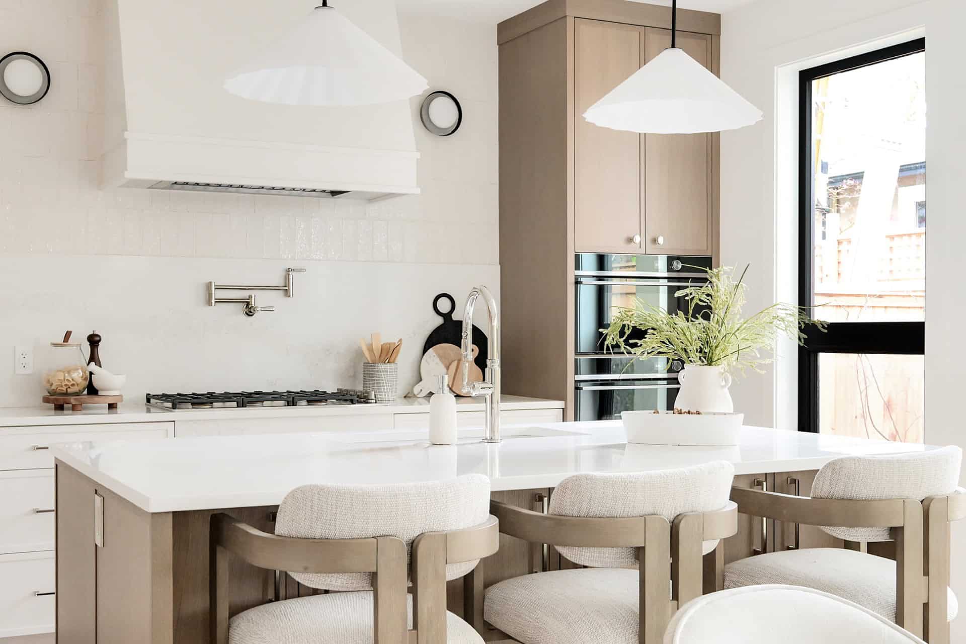 Modern white kitchen with island, pendant lights, and bar seating in Victoria BC home by White Wolf Homes.