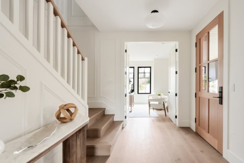Bright, inviting entry hall with white paneled walls and warm wood door in a Victoria BC custom home.