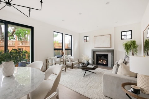 Bright living room with large windows, modern neutral furniture, and a fireplace in a white-toned Victoria BC home.
