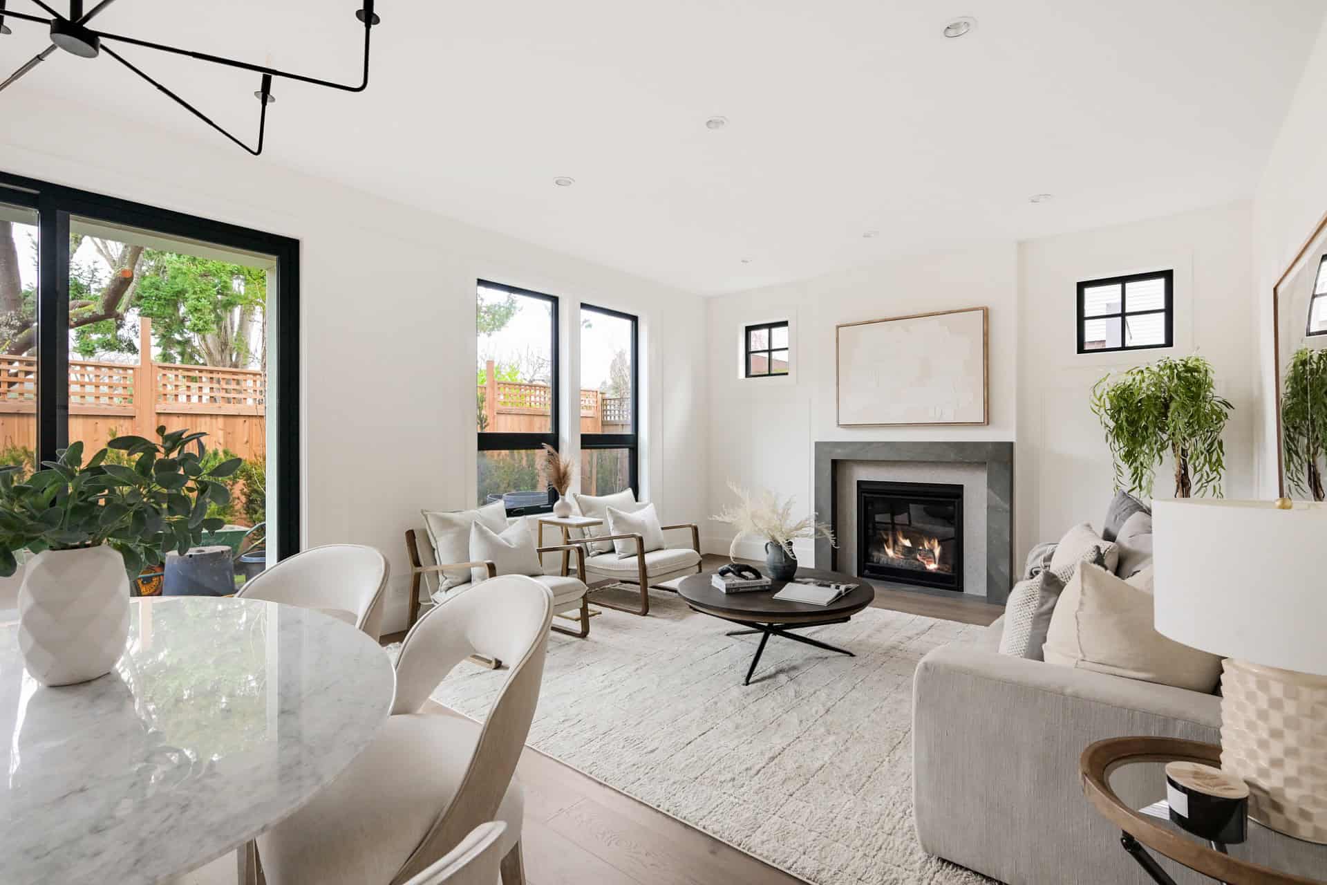 Bright living room with large windows, modern neutral furniture, and a fireplace in a white-toned Victoria BC home.