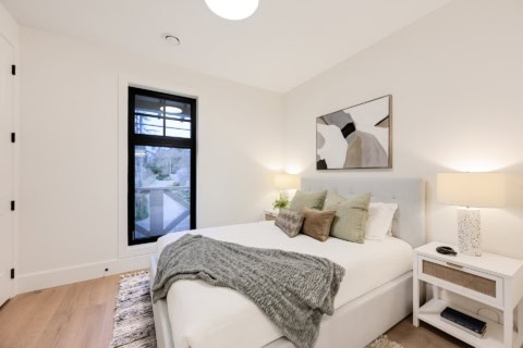 Bedroom of a modern white-and-beige home with a large window, cozy bed, and soft lighting.