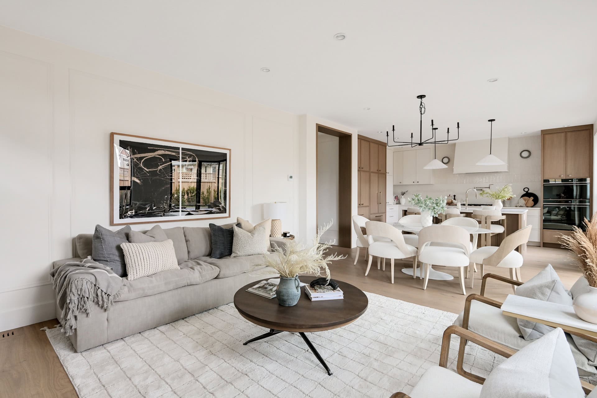 Modern living room with light gray sofa, round coffee table, and open kitchen in a bright, airy home.