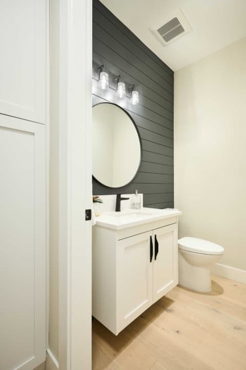 Modern bathroom with white vanity, round mirror and dark shiplap wall.