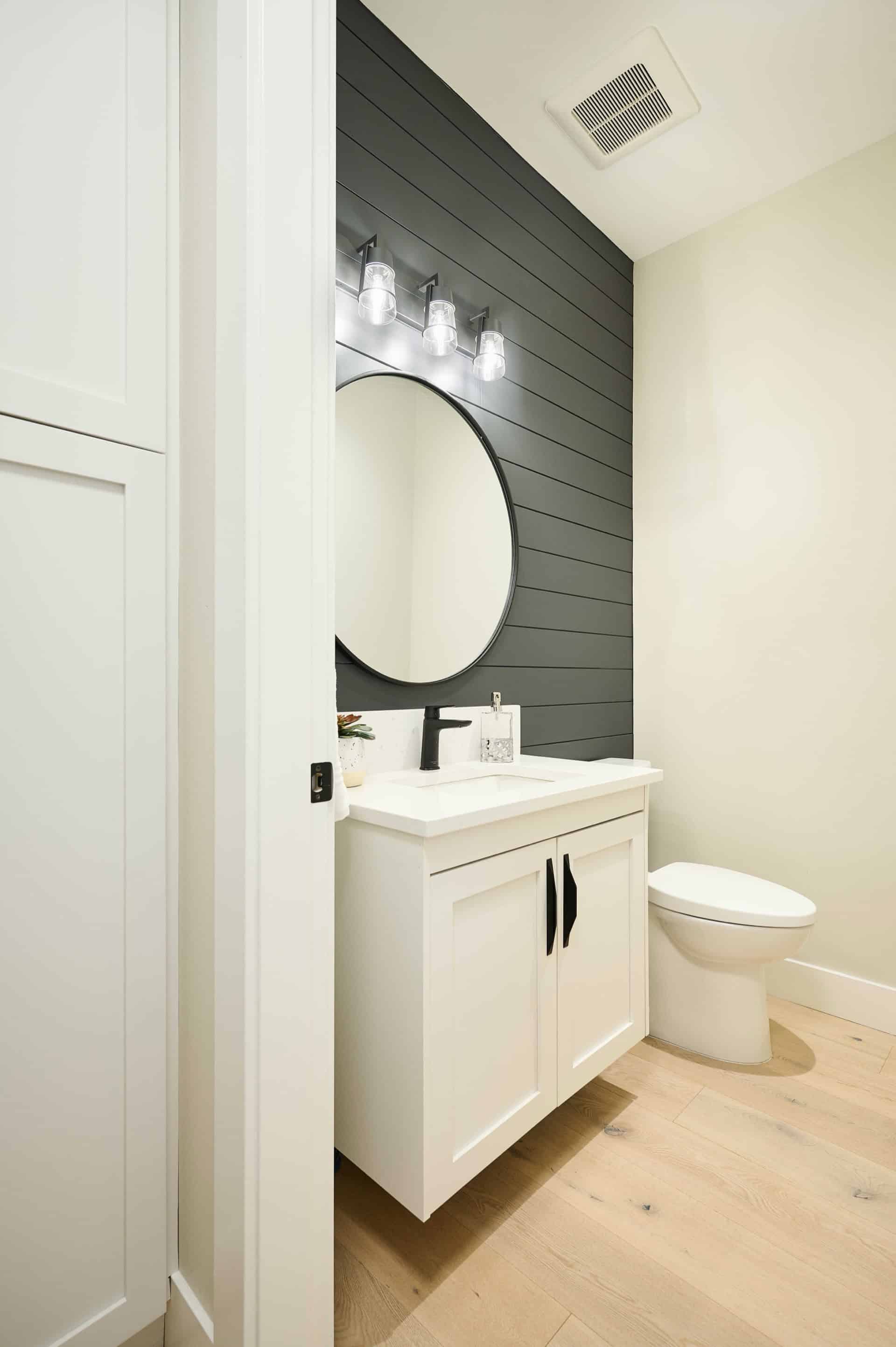 Modern bathroom with white vanity, round mirror and dark shiplap wall.