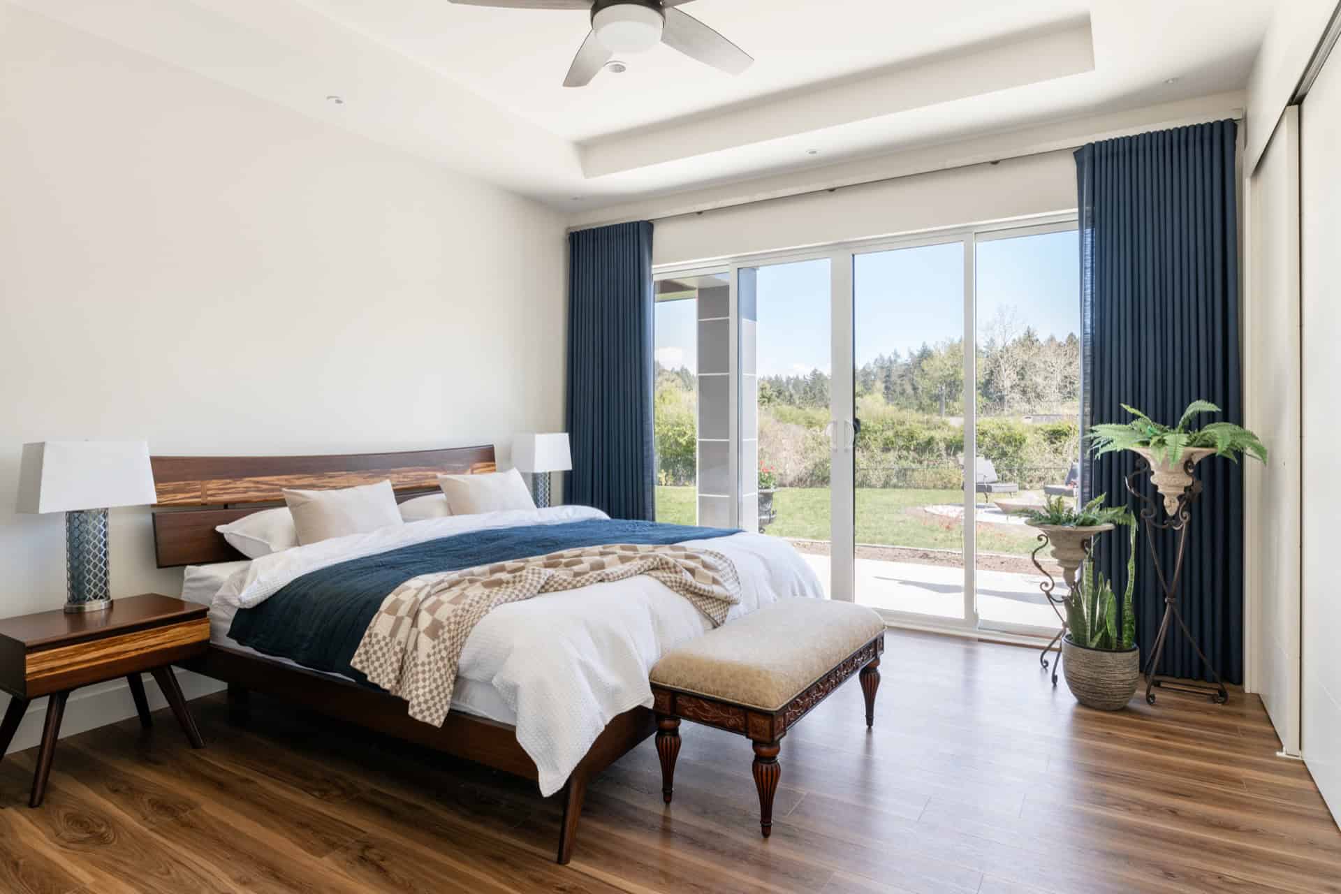 Bright master bedroom with large glass doors to a garden and blue curtains.