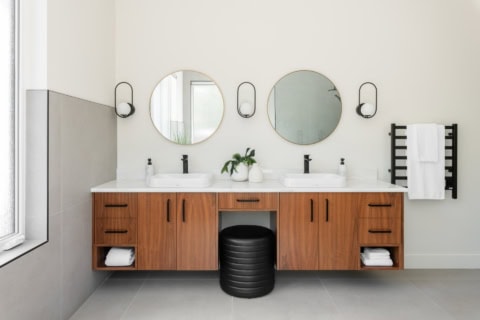 Modern bathroom with dual sinks, wooden vanity, circular mirrors and black wall sconces.