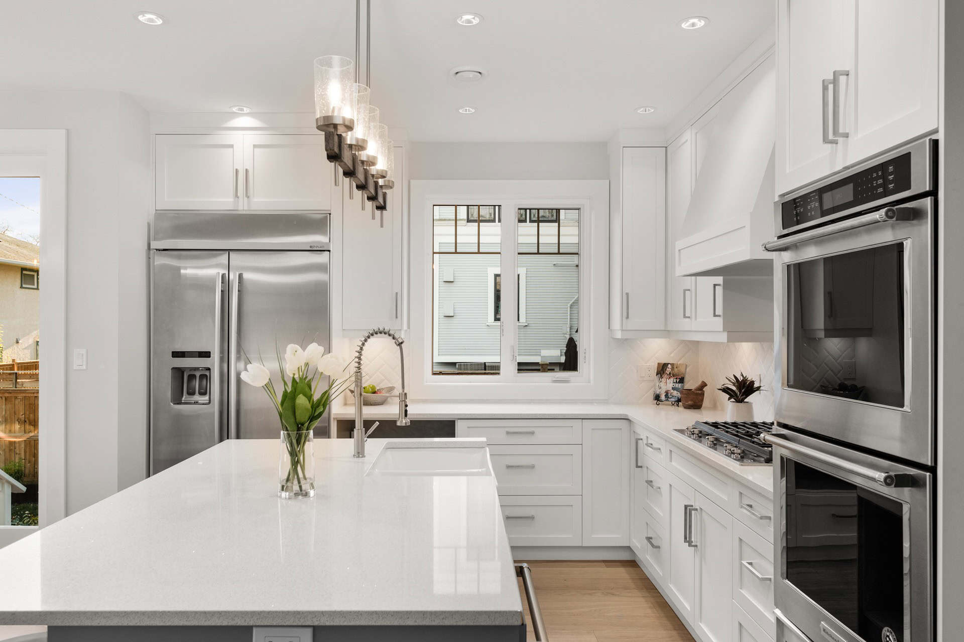 Bright white kitchen with island, stainless steel appliances, and modern pendant lights.