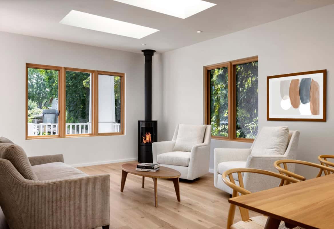 Bright living room with large windows, modern wood furniture, and a wood-burning stove in Victoria BC.