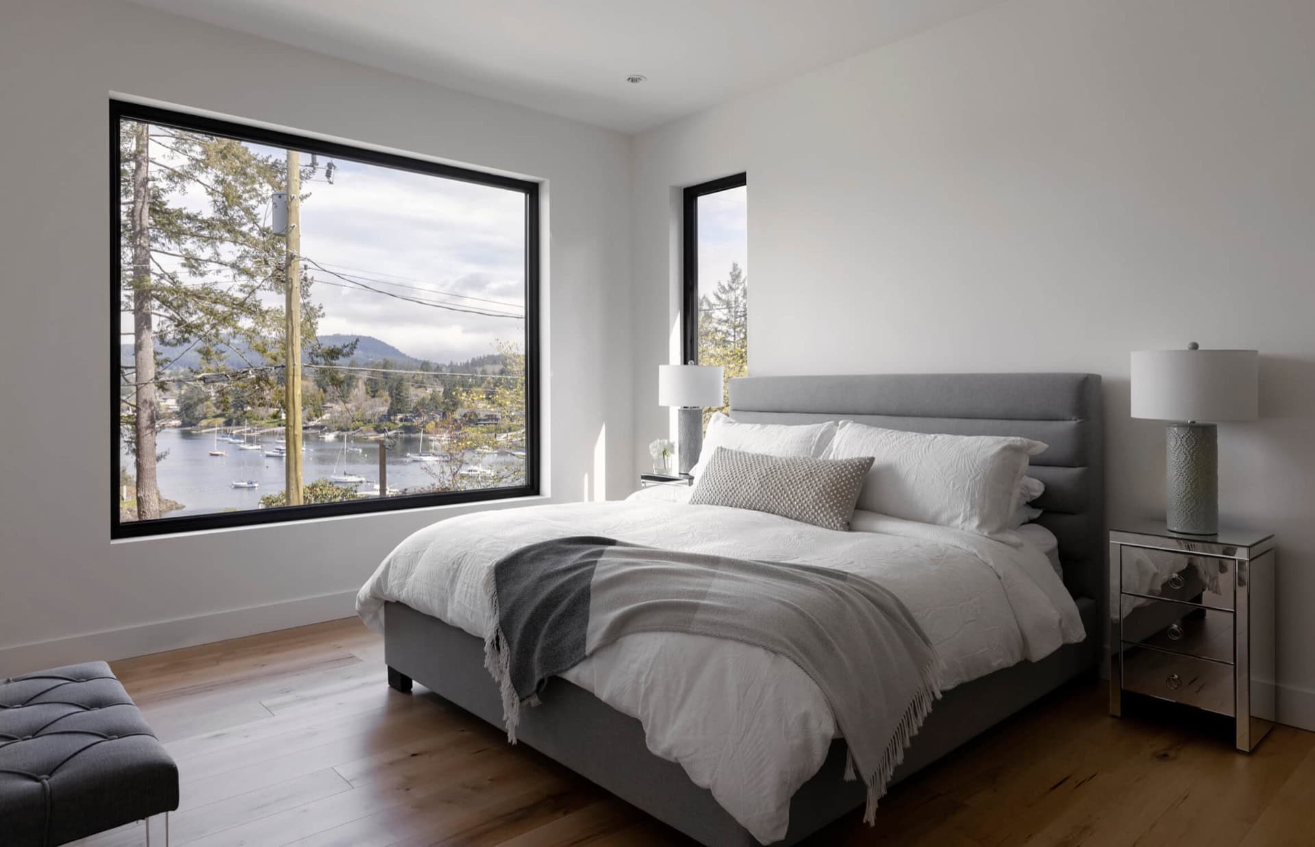 Bright modern bedroom with large windows overlooking water and trees.