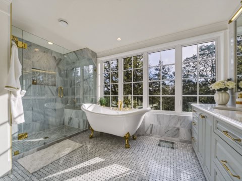 Elegant marble bathroom with freestanding clawfoot tub and large windows in Victoria BC home.