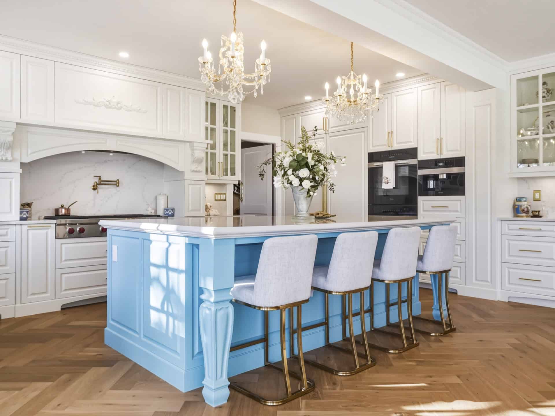 Bright kitchen with white cabinetry and a blue island featuring gold legs and four upholstered bar stools.