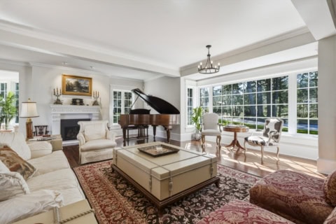 Bright living room with grand piano, cream seating, and large windows in The Parkwood Estate.