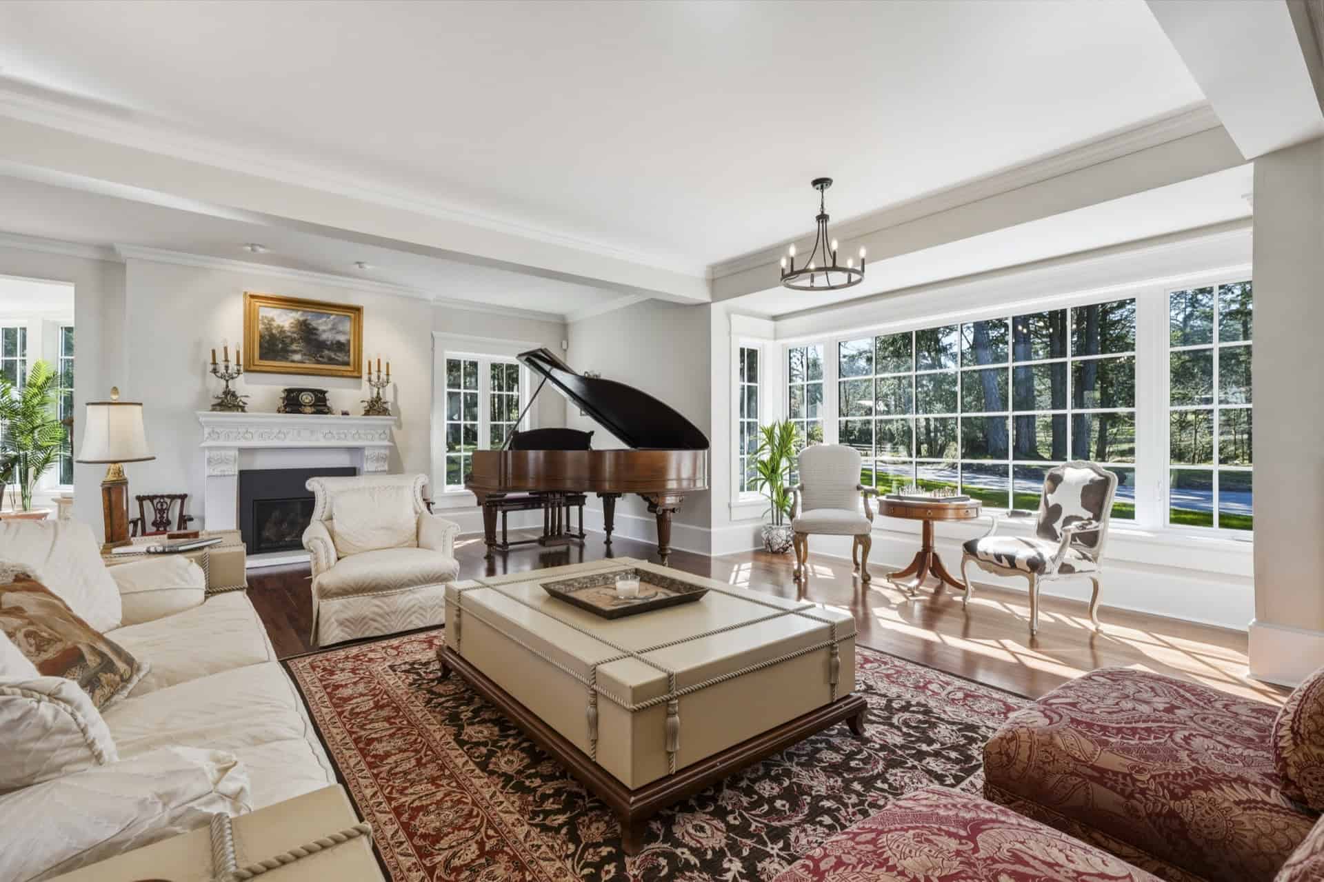 Bright living room with grand piano, cream seating, and large windows in The Parkwood Estate.