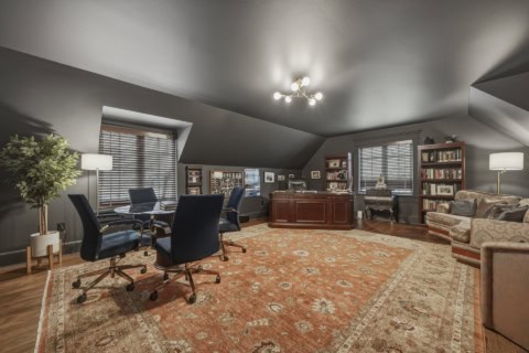 Interior of a luxury home office with dark walls, wooden desk, seating, bookshelves and warm lighting.