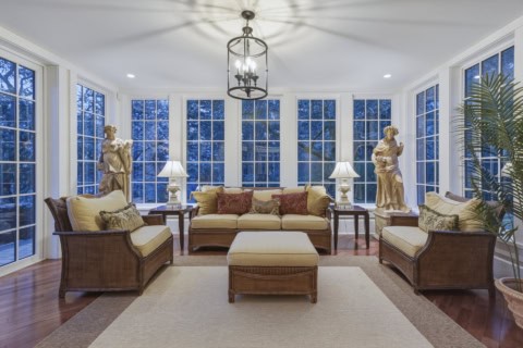 Bright sunroom with wicker sofas, cream cushions, statues, and large windows at The Parkwood Estate.