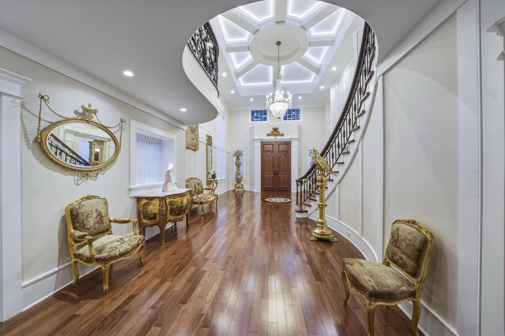 Elegant Victorian-inspired foyer with curved staircase, ornate chairs, and chandelier in The Parkwood Estate.