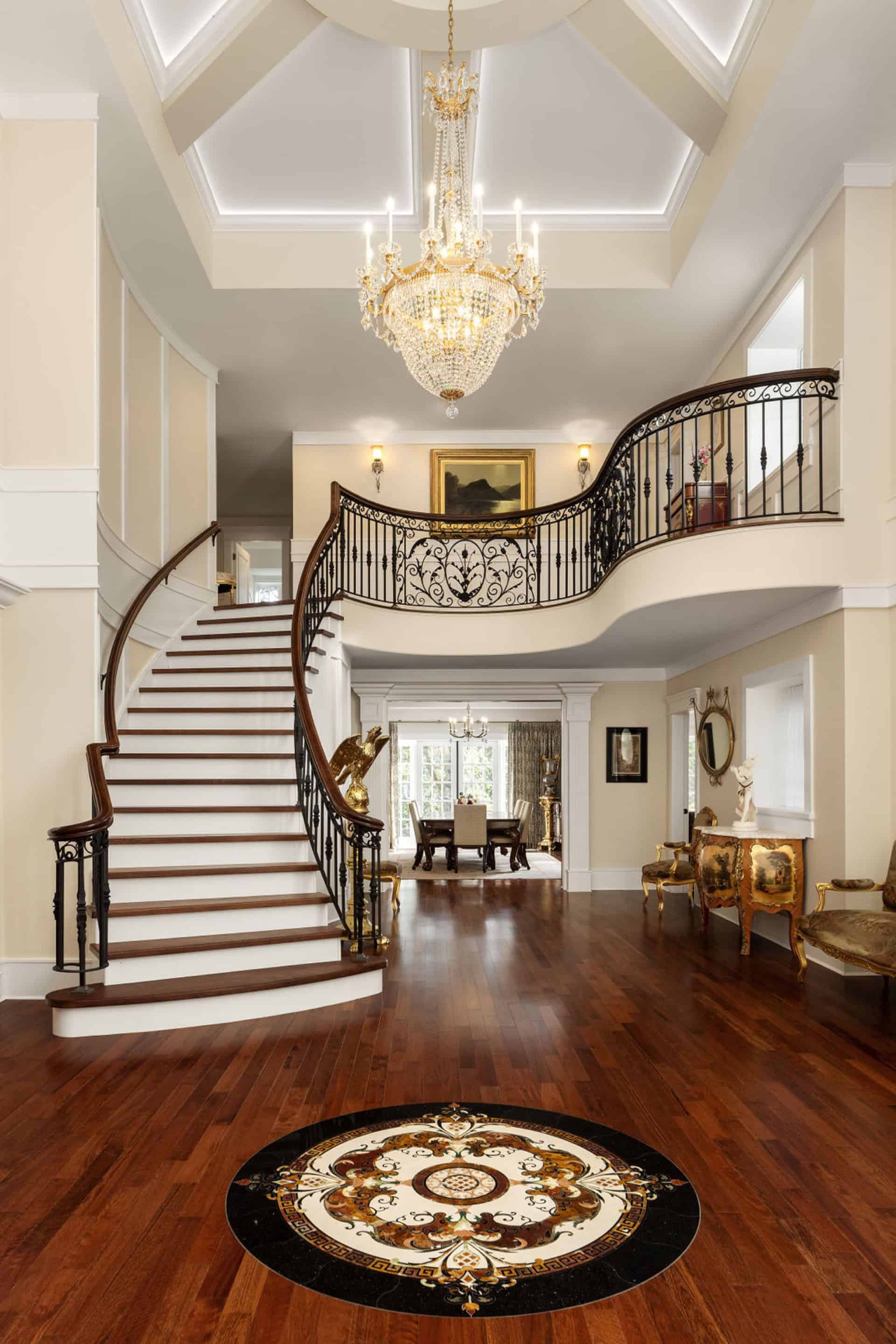 Elegant grand foyer with sweeping curved staircase and chandelier in a luxurious Victorian-style home.