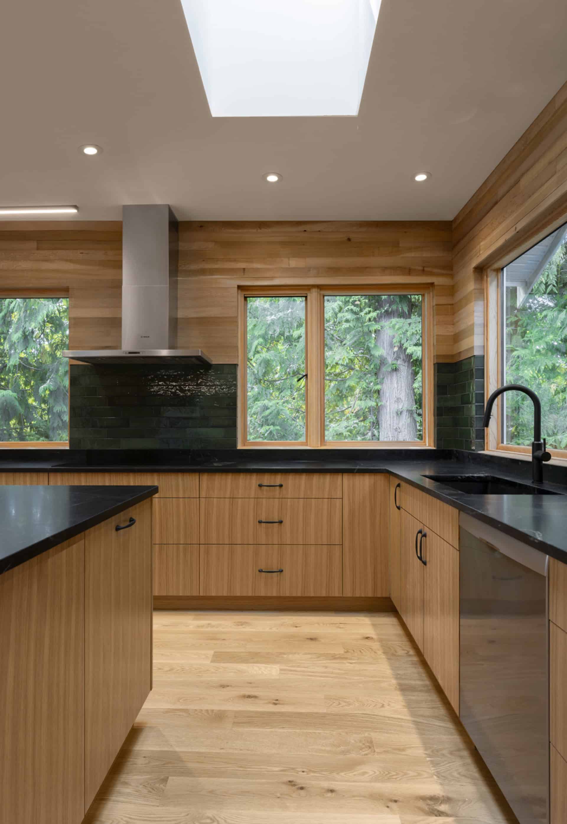 Modern kitchen with wooden cabinets, black countertops, and skylight in Victoria BC home by White Wolf Homes.