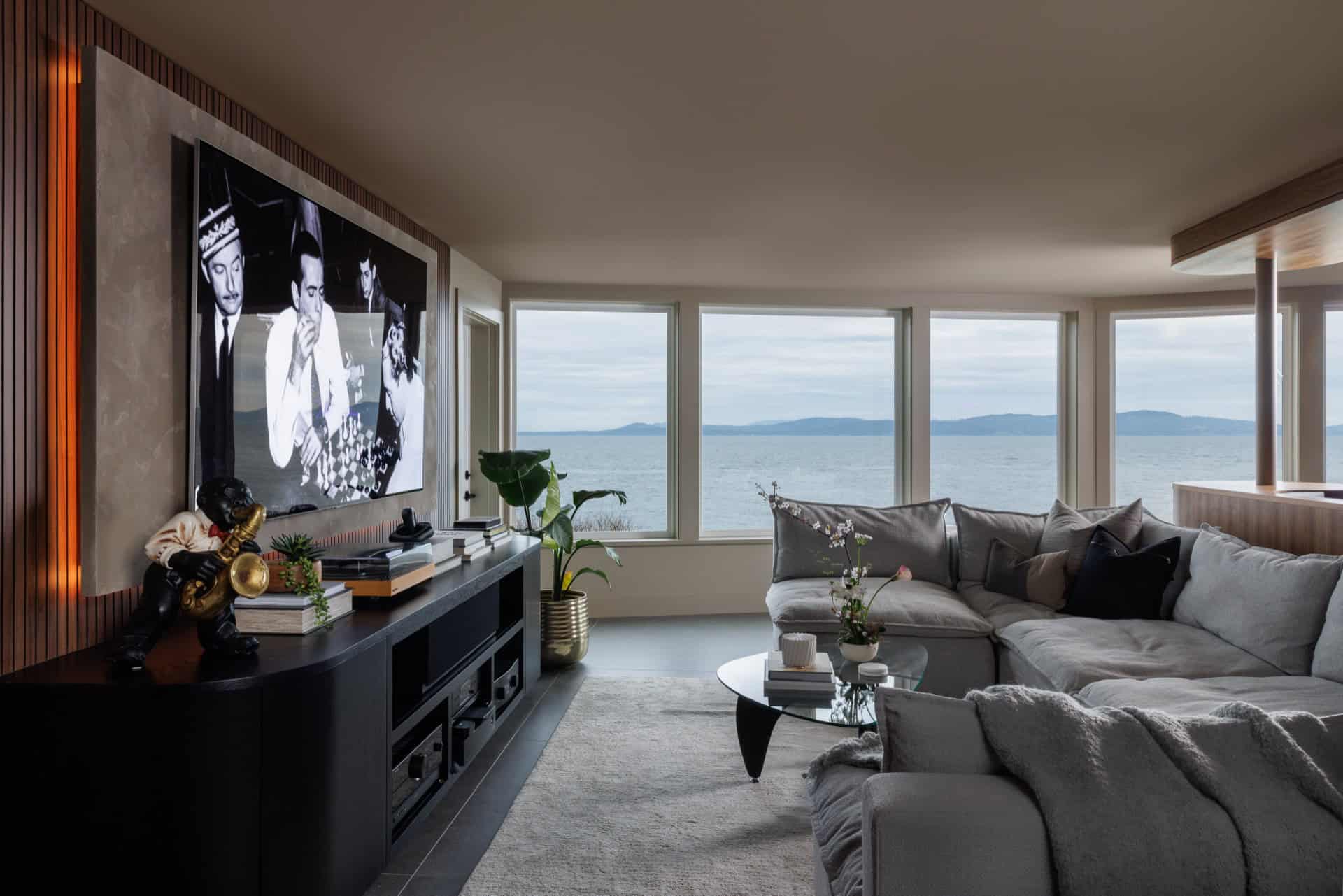 Modern living room with large windows overlooking a coastal landscape and grey sectional sofa.