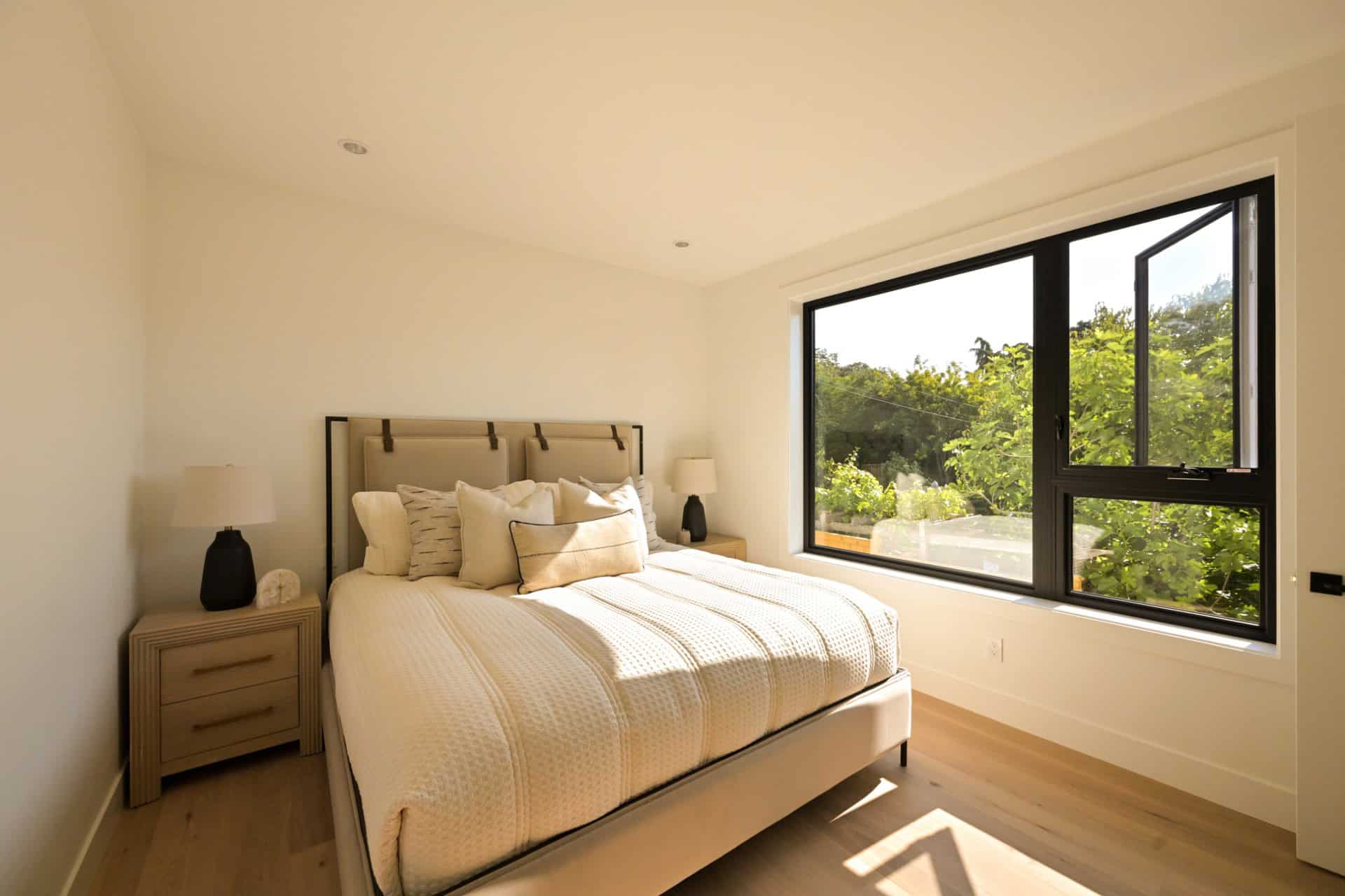 Bright airy bedroom with large window overlooking greenery and a neutral-toned bed.