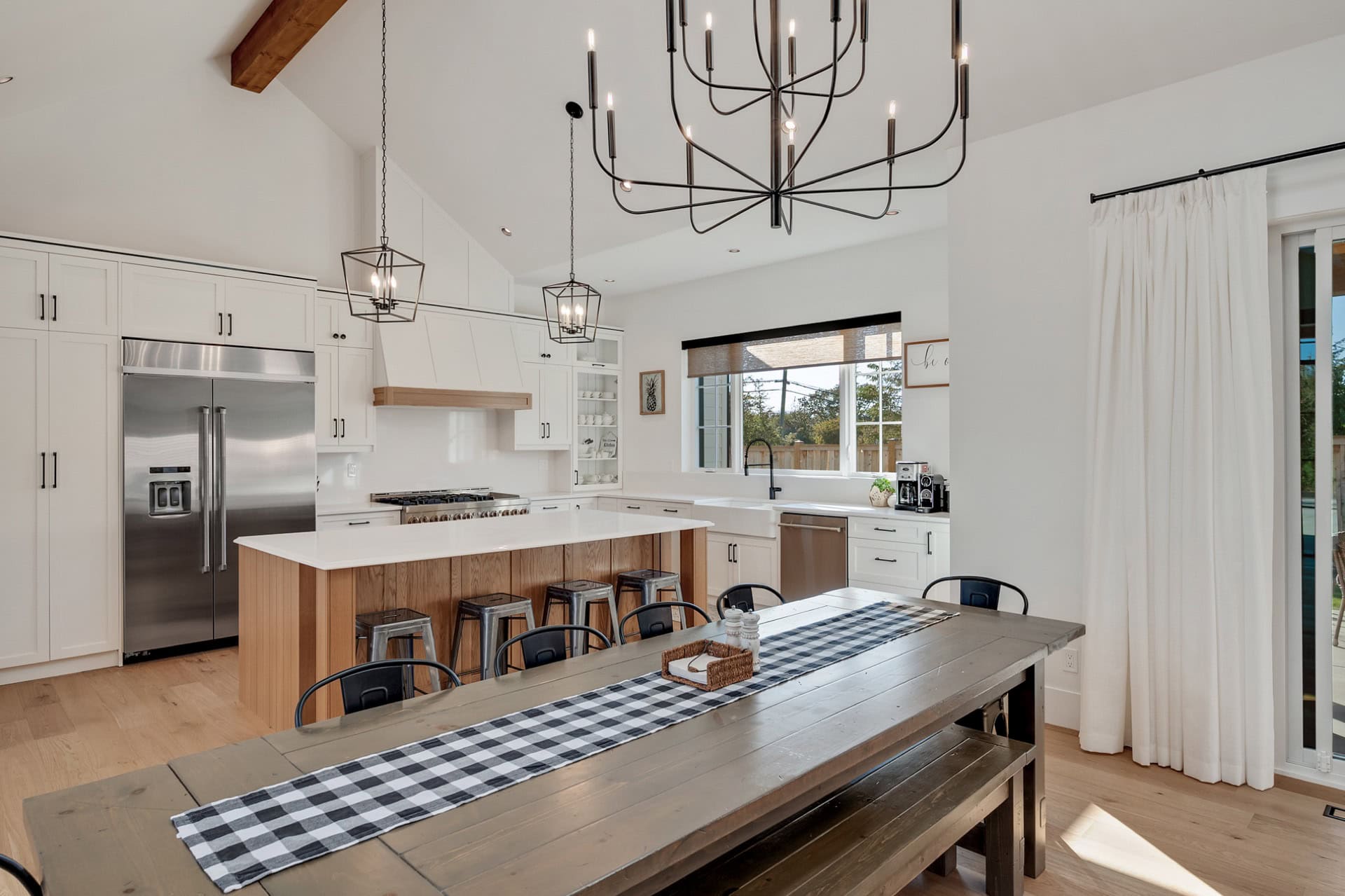 Modern open-concept kitchen with island, white cabinets, and rustic dining table.