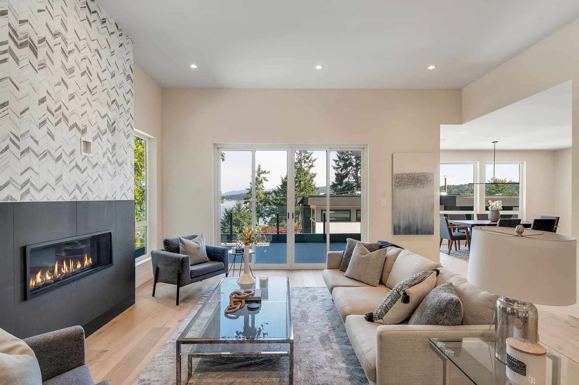 Living room with fireplace, modern seating, large windows showing outdoor scenery, and contemporary decor.
