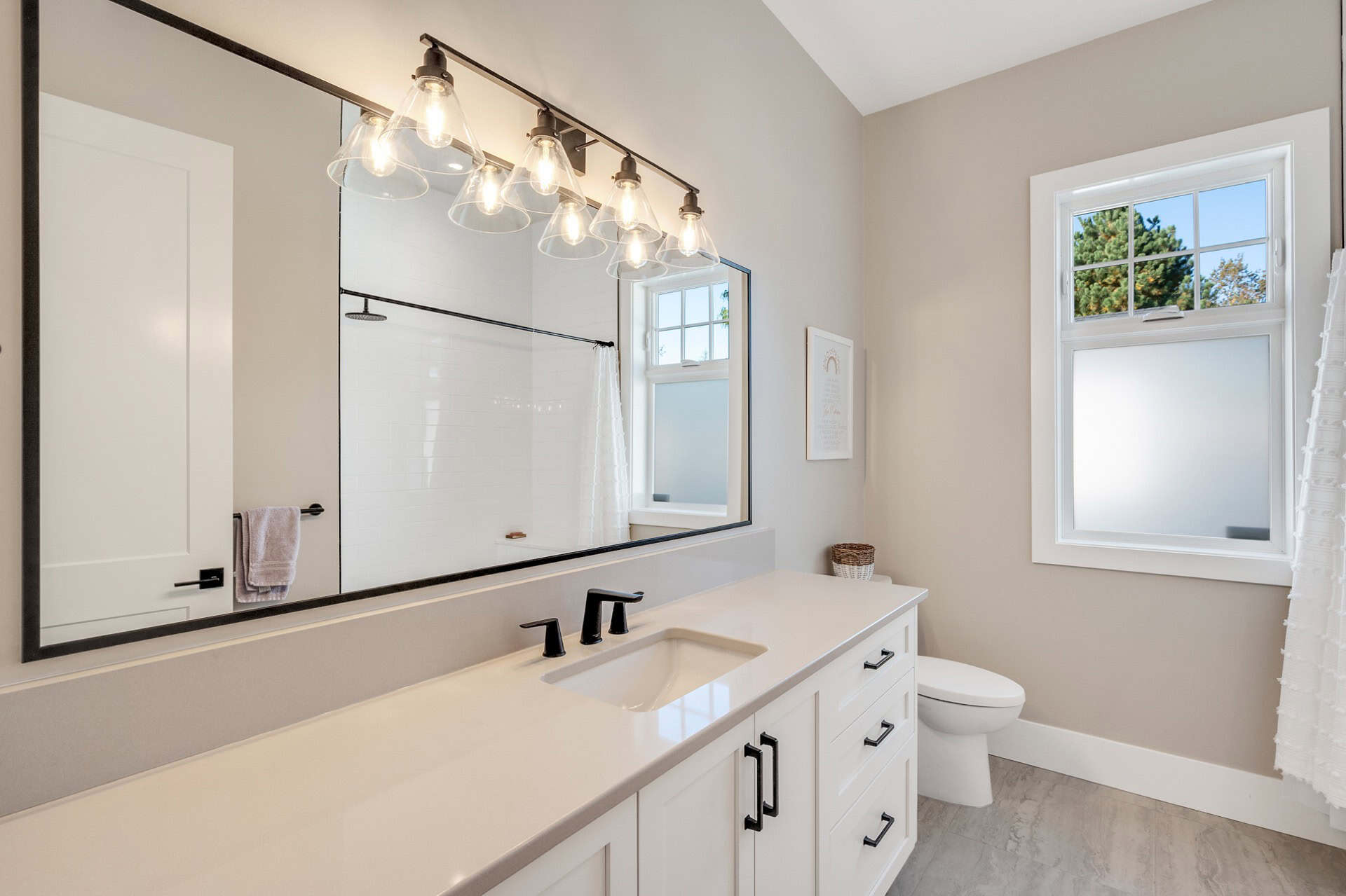 Bright modern bathroom with double vanity, large mirror and window.