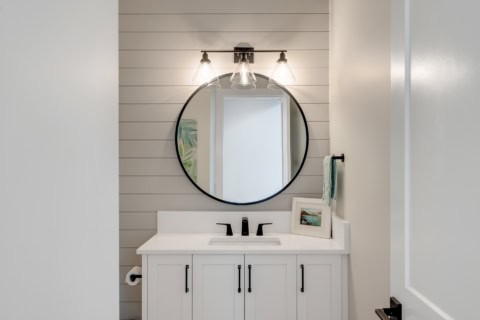 White Wolf Homes bathroom vanity with round mirror and shaker cabinets.