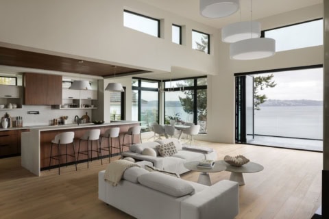 Bright open-concept living area with large windows and waterfront view, modern kitchen in white and cream.
