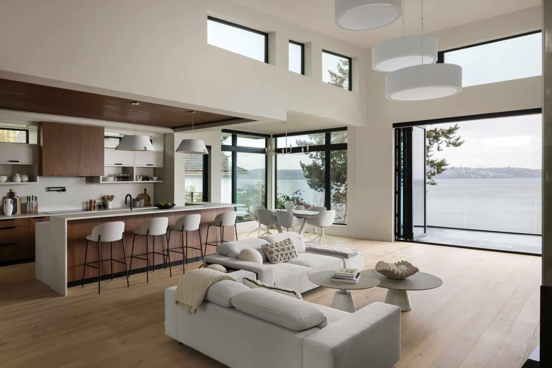 Bright open-concept living area with large windows and waterfront view, modern kitchen in white and cream.