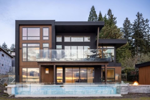 Modern two-story custom home with large glass facade and balcony over a pool.