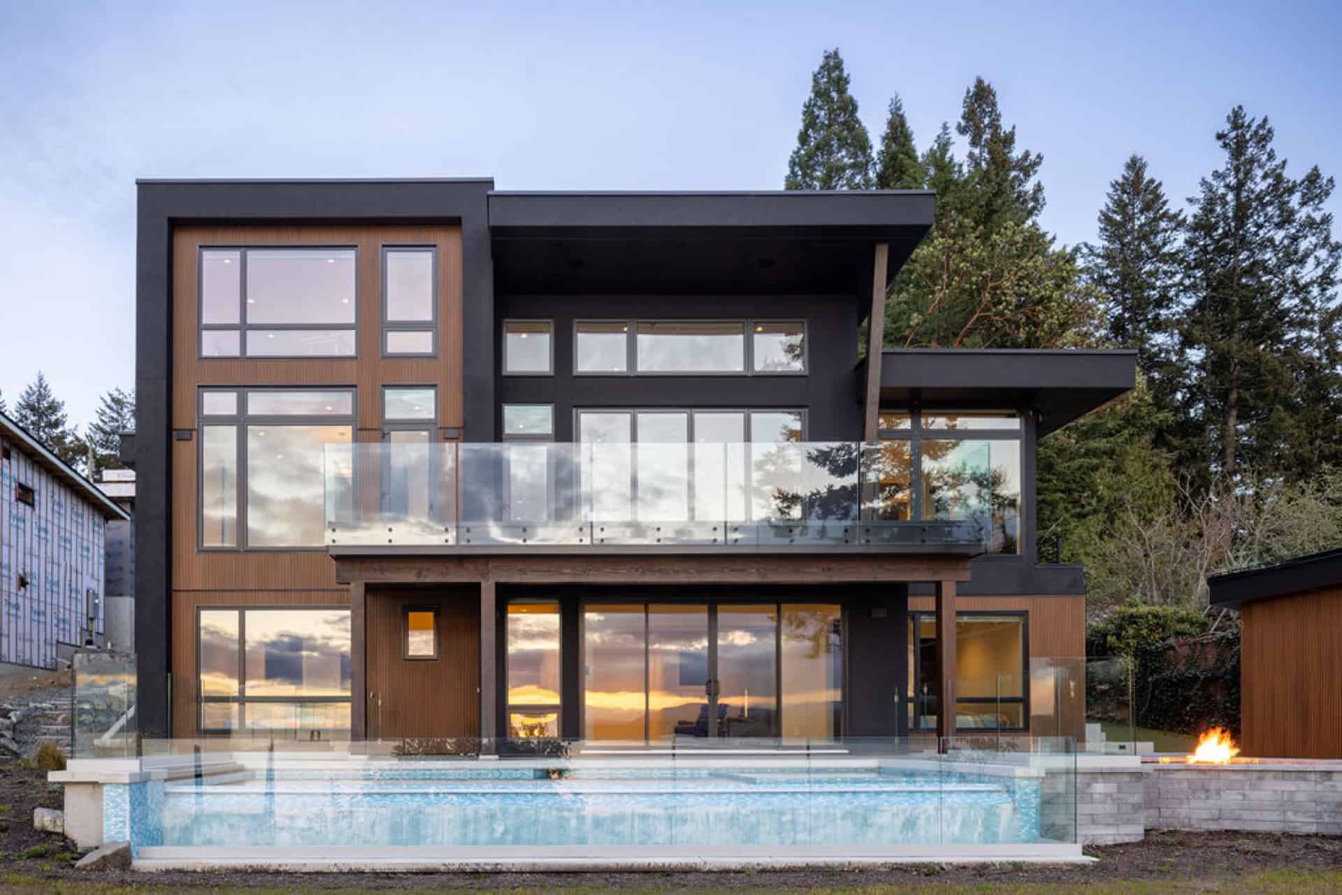 Modern two-story custom home with large glass facade and balcony over a pool.