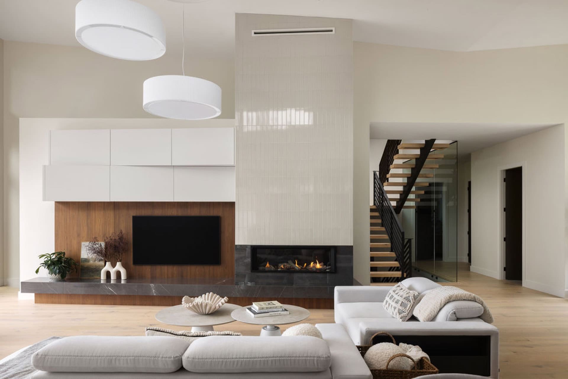 Modern living room with fireplace, white cabinets, and a staircase in Victoria BC home.